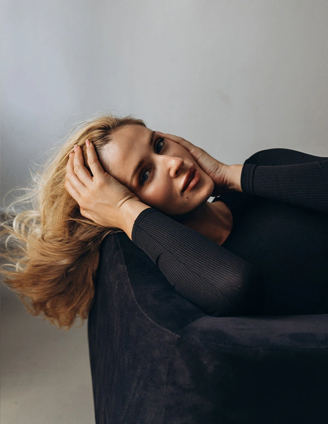 Blonde woman in black top lying down with hand in hair against white background in fashion portrait - Chemical peels in Alpharetta, GA