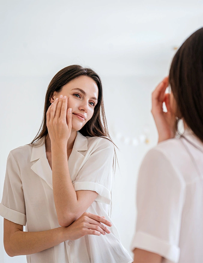 Woman examining her face in mirror touching skin checking skincare routine and complexion - Glo2facial in Alpharetta, GA
