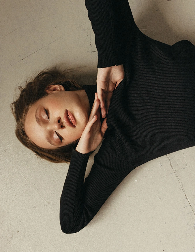Woman in black turtleneck lying down with natural makeup and curly hair against white background - Kybella in Alpharetta, GA