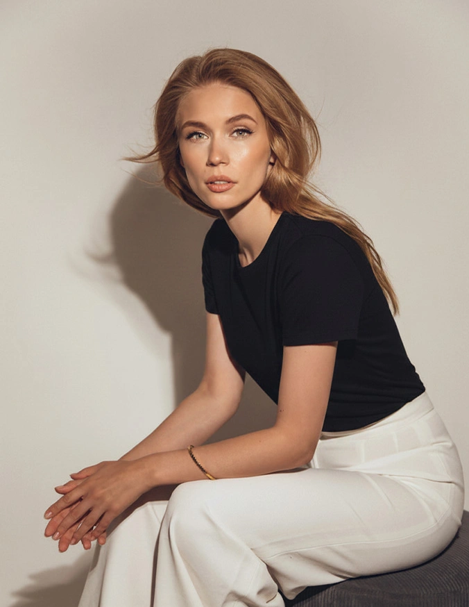 Woman in black shirt and white pants sitting against neutral wall with warm lighting - Peptides in Alpharetta, GA
